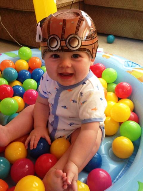 A child sits in a ball pit wearing a vinyl helmet