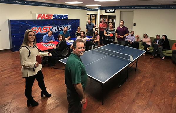 A FASTSIGNS team spends time together in a break room while playing games